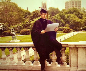 Doug sitting on railing in graduation robes