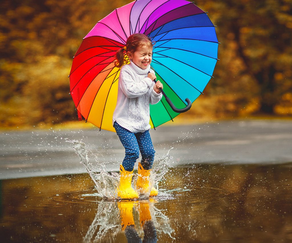little girl with brightly colored umbrella splashing on a big puddle