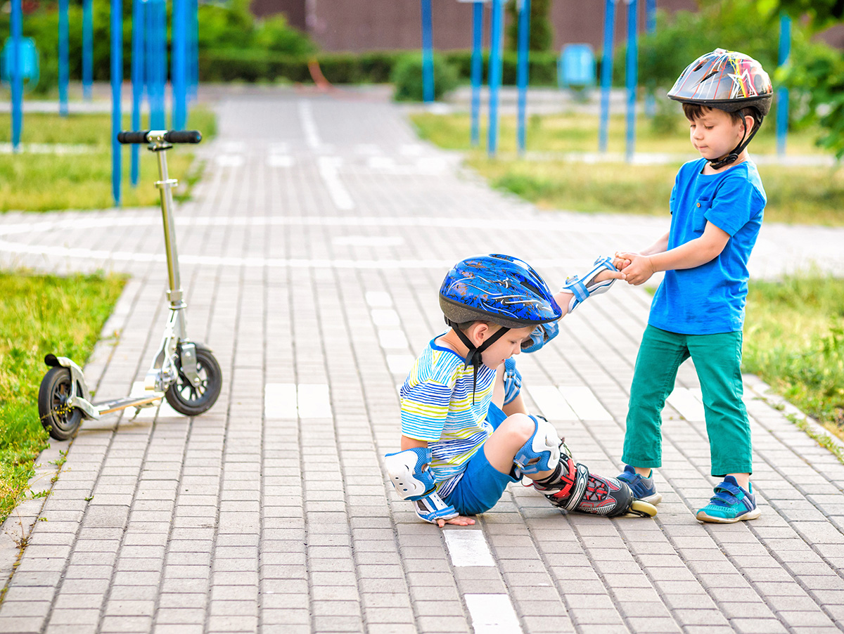 Young child helping up another after falling off roller blades