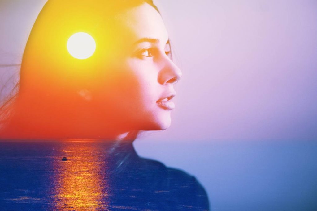 Young woman's head looking right superimosed over an ocean sunset