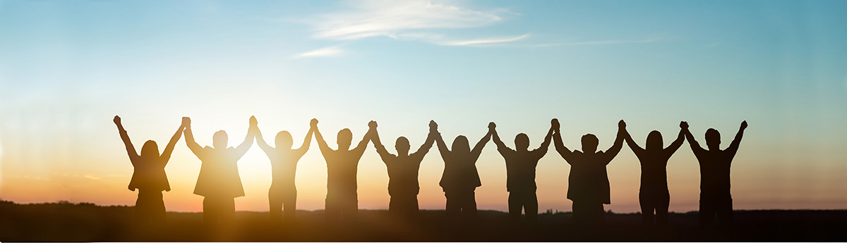a line of 10 people holding hands raied over their heads, silhouetted by the sunset