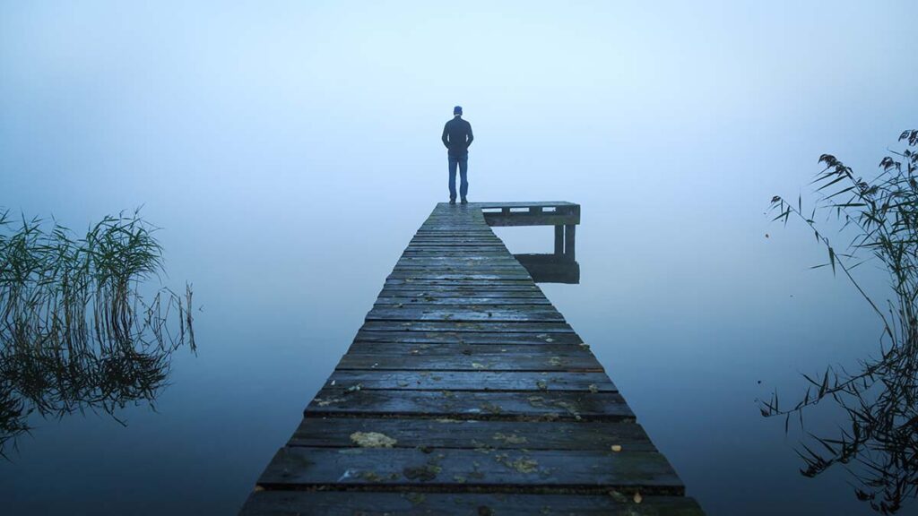 Person standing at end of long dock, alone, silent